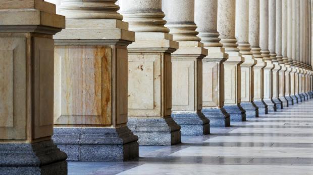 A row of marble columns with the sunlight shining through, casting shadows on the floor