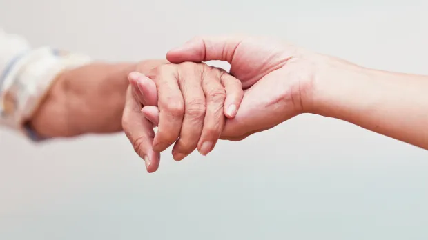 A younger carer holds the hand of an older man or woman